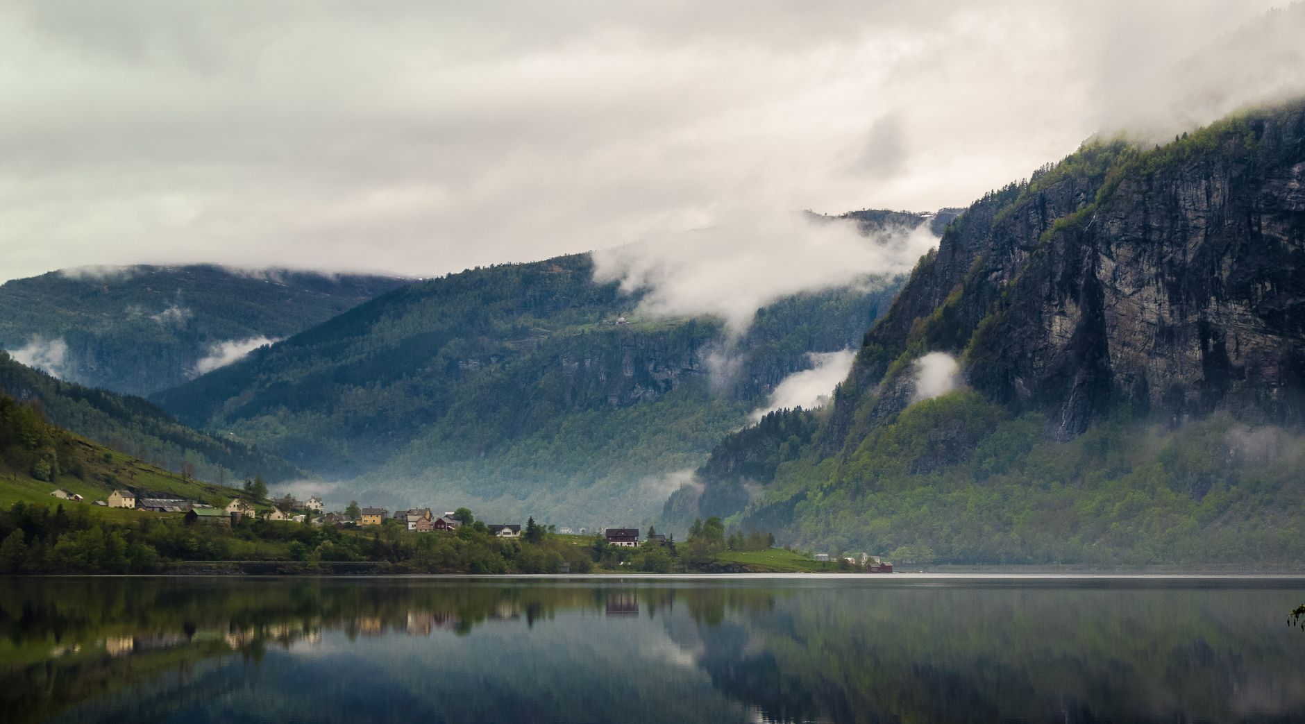 Deep indigo fjord reflecting vertical cliff walls under morning fog